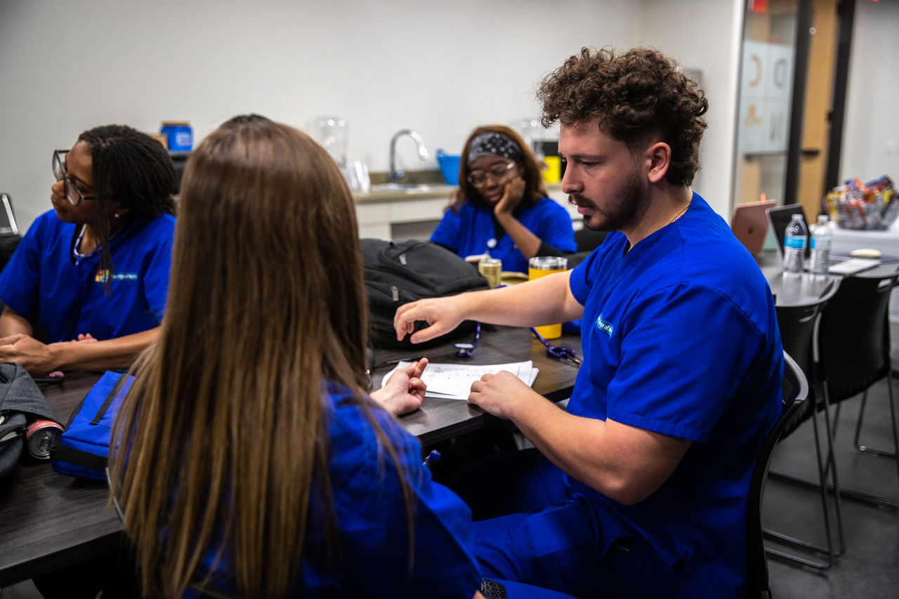 Medical students in blue scrubs gather in classroom
